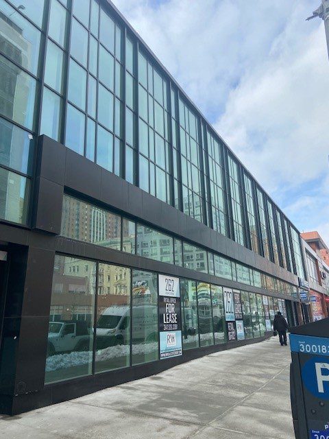 Modern commercial building with glass facade and "for lease" signs on the ground floor.
